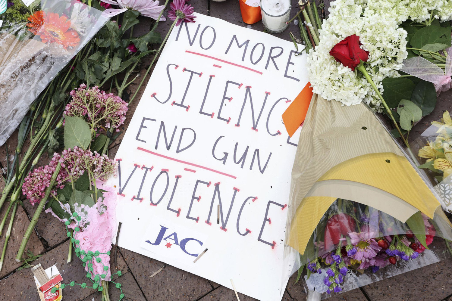 A sign saying "No more silence, end gun violence" sits next to flowers and candles at the corner of Central and St. Johns avenues in Highland Park, Illinois, on July 6, 2022, as a memorial honoring the victims of the Fourth of July parade mass shooting. (Antonio Perez/Chicago Tribune/TNS)