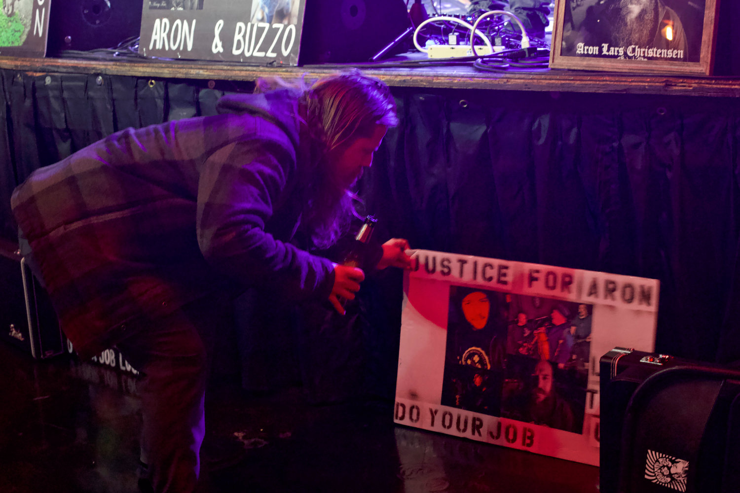 A concertgoer helps fix a sign that reads “Justice for Aron” and “Do Your Job” at a 50th birthday celebration for Aron Christensen held at Dante’s in Portland on Friday.