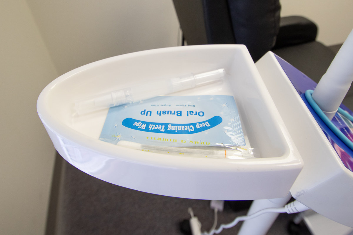 A 16% hydrogren peroxide gel, applicator and teeth cleaning wipe are displayed on the blue LED light stand used to accelorate the teeth whitening process.