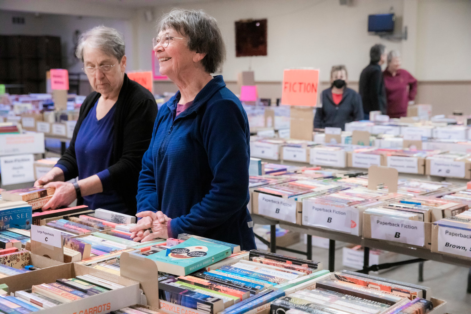 Jo Martinez smiles alongside Renae Seegmiller while setting up the AAUW Used Book Sale at the Moose Lodge in Centralia on Tuesday.