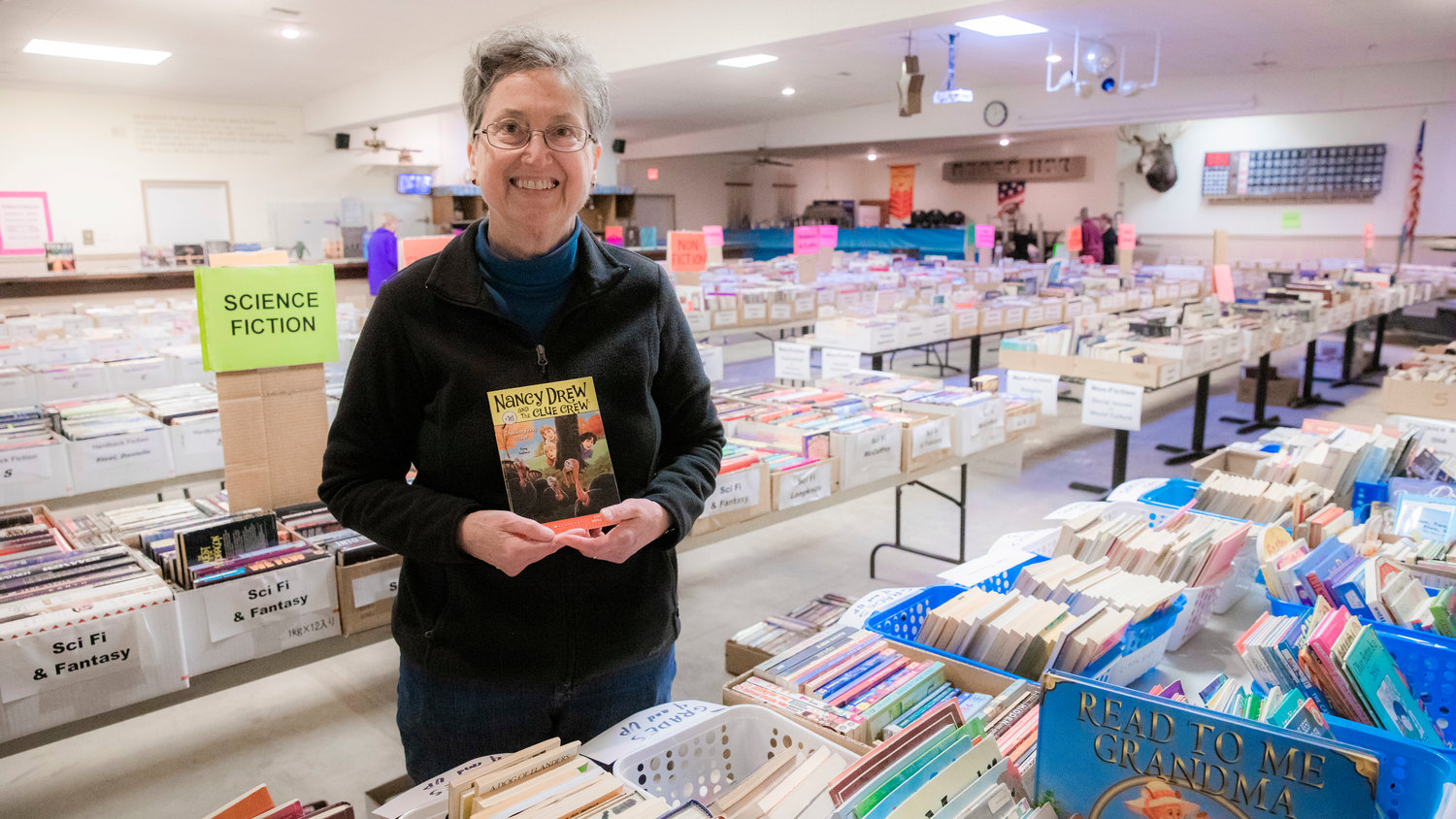 Laura Hewett, a former teacher in the Chehalis School District, smiles and holds up books she would show students on display at the AAUW Used Book Sale at the Moose Lodge in Centralia on Tuesday.