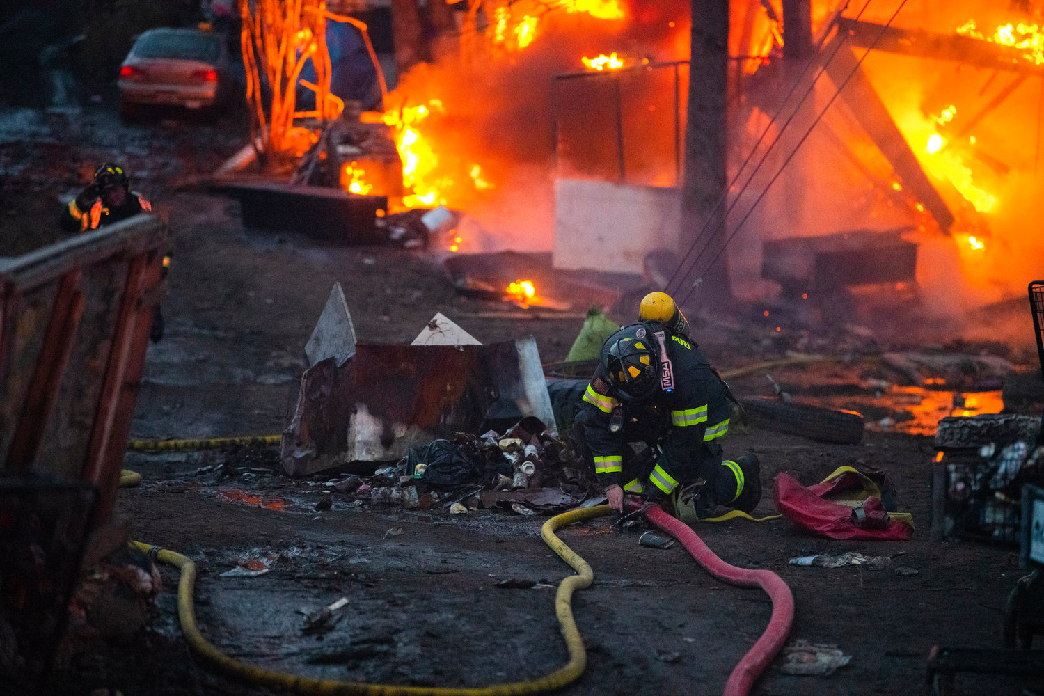 Firefighters stretch and link hoses to reach a burning structure inside a homeless encampment near Blakeslee Junction as flames consume debris Tuesday, March 28, 2023.