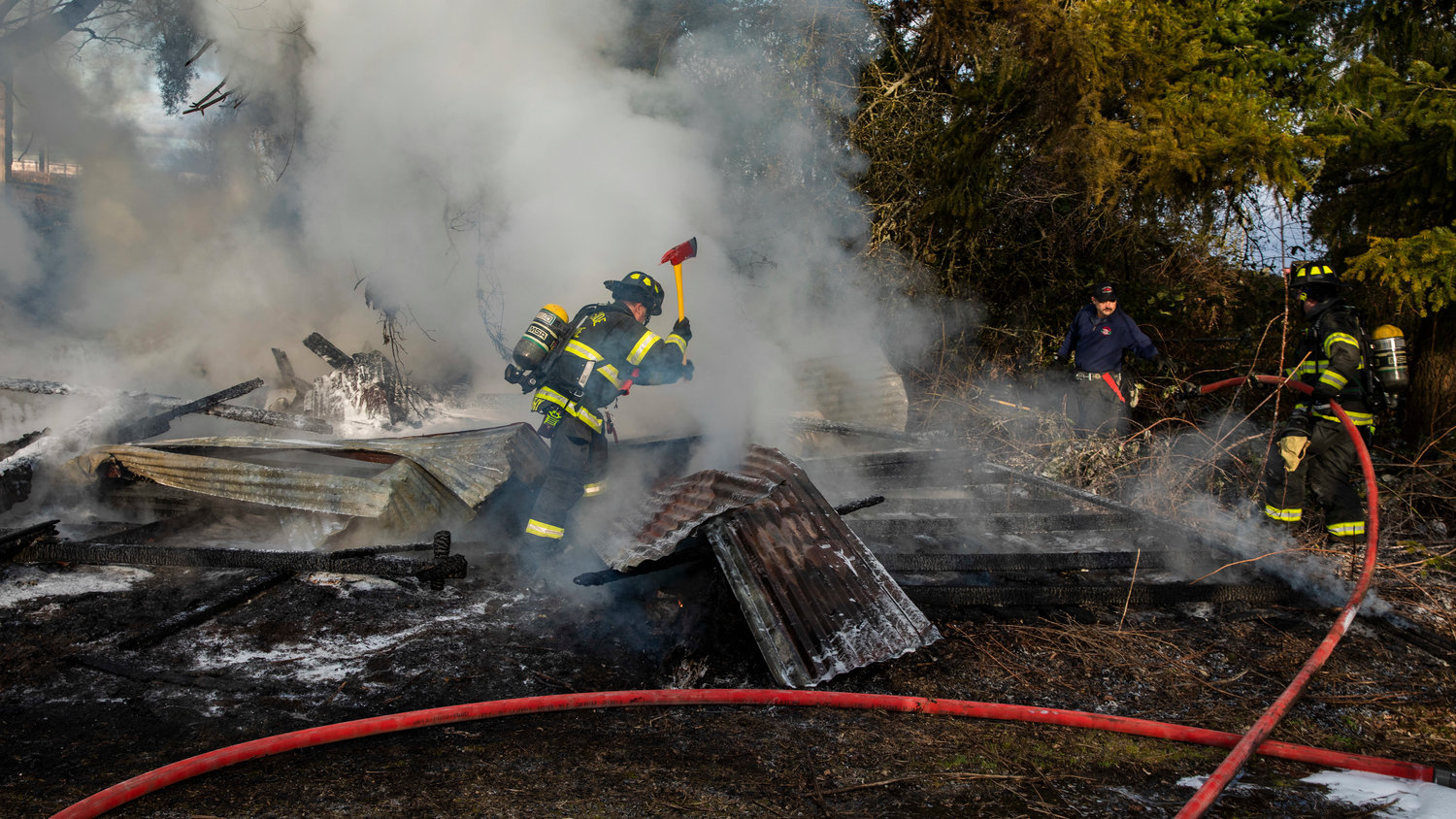 Captain Casey McCarthy, with Riverside Fire Authority, uses an ax to break down debris after flames destroyed an outbuilding that was supposed to be unoccupied along Long Road in Centralia Thursday morning.