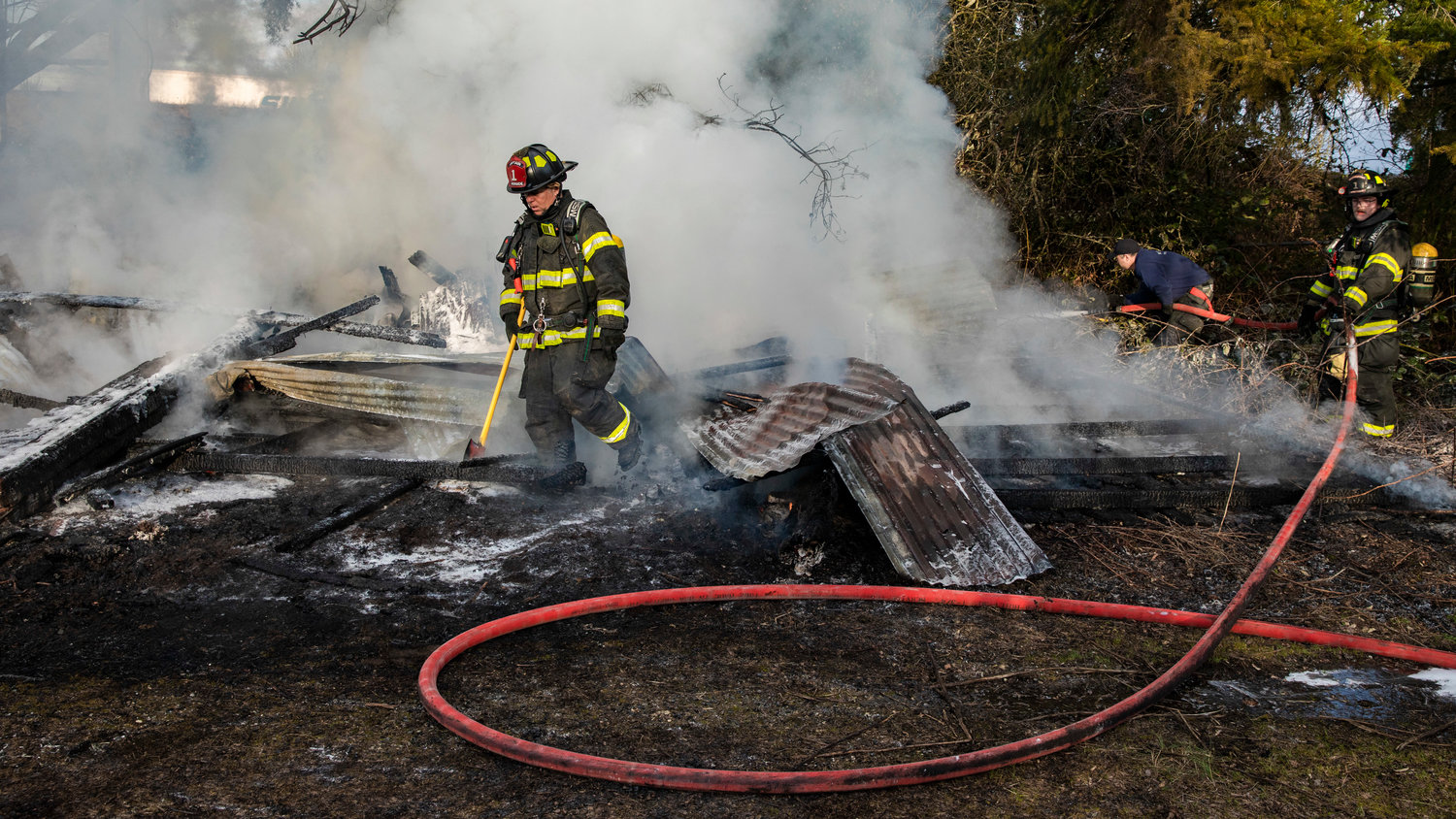 Captain Casey McCarthy, with Riverside Fire Authority, walks away from smoky debris while using an ax after flames destroyed an outbuilding that was supposed to be unoccupied along Long Road in Centralia Thursday morning.
