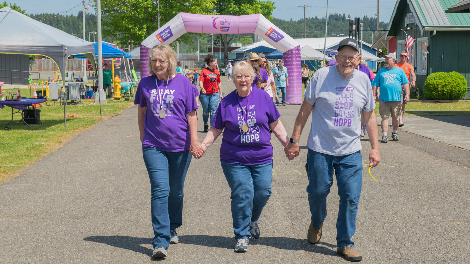 Survivor Katie Foss, center, holds hands with her husband John, right, and other participants in a Relay For Life walk at the Southwest Washington Fairgrounds on Saturday, May 20.