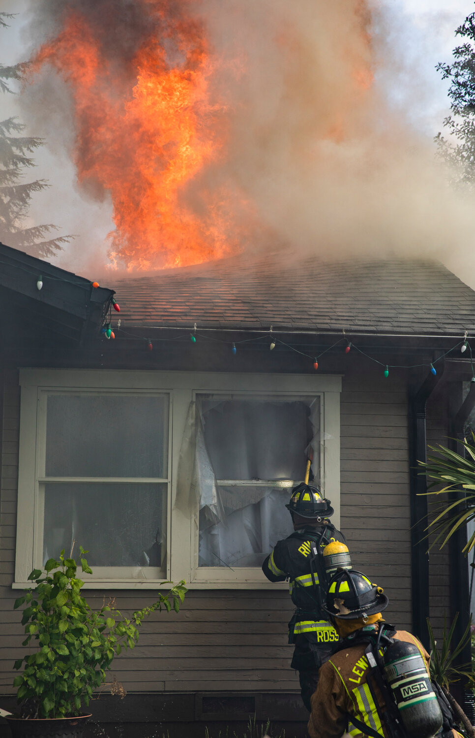 A Riverside firefighter uses an ax to break windows at a residence in the 800 block of Centralia College Blvd. as flames rise from the roof on Wednesday, May 24.
