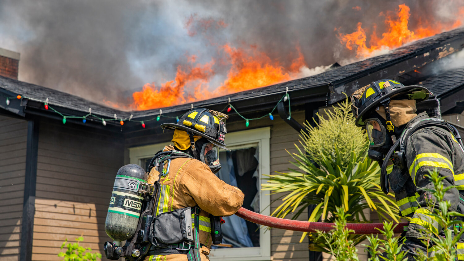 Lewis County and Riverside firefighters carry hoses and work to put out flames at a residence in the 800 block of Centralia College Blvd. on Wednesday, May 24.