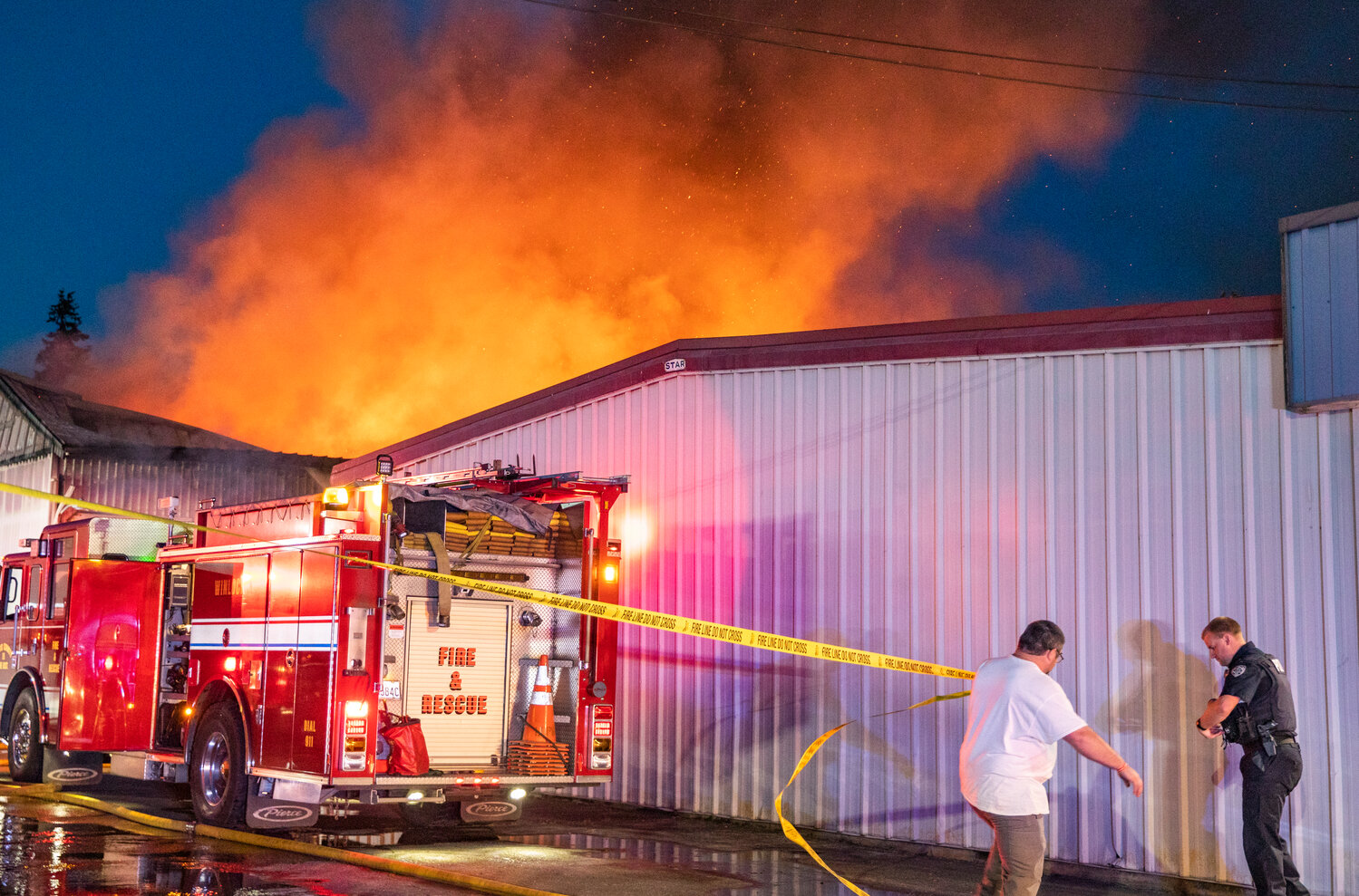 Napavine residents help first responders string up caution tape as a massive blaze escapes the roof of a storage building in downtown on Saturday, June 3.