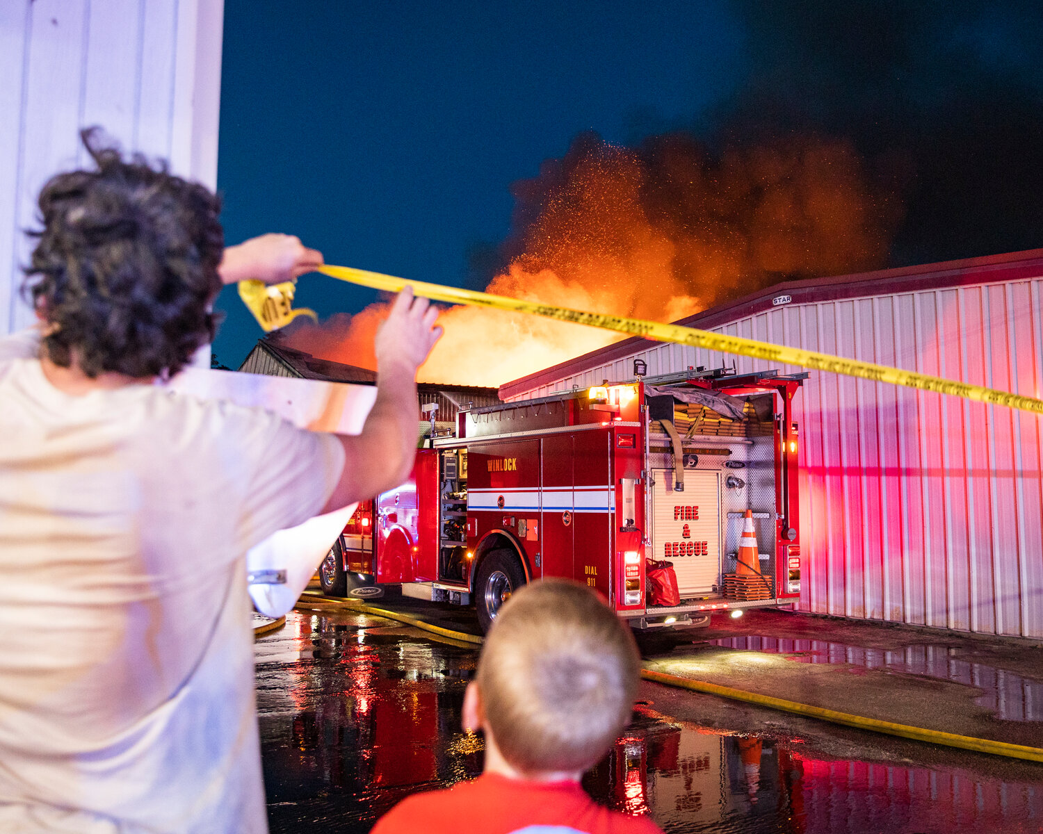 Napavine residents help first responders string up caution tape as a massive blaze escapes the roof of a storage building in downtown on Saturday, June 3.