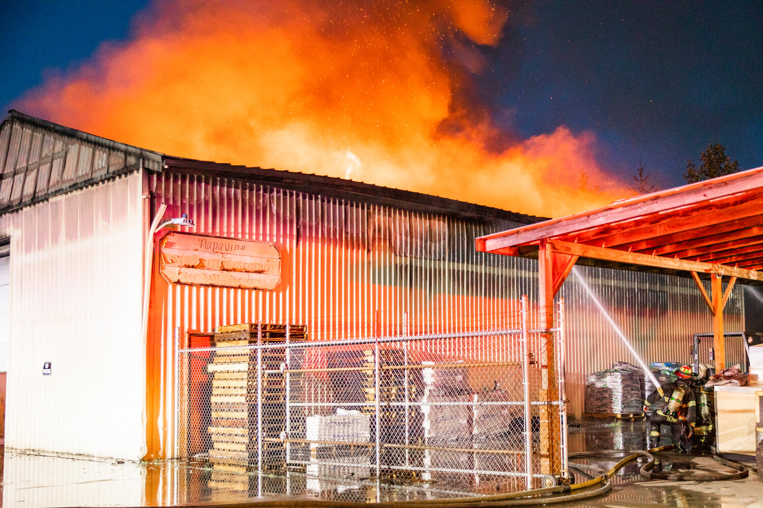 Firefighters push back flames breaking out of the top of an aluminum storage building in Napavine on Saturday night.