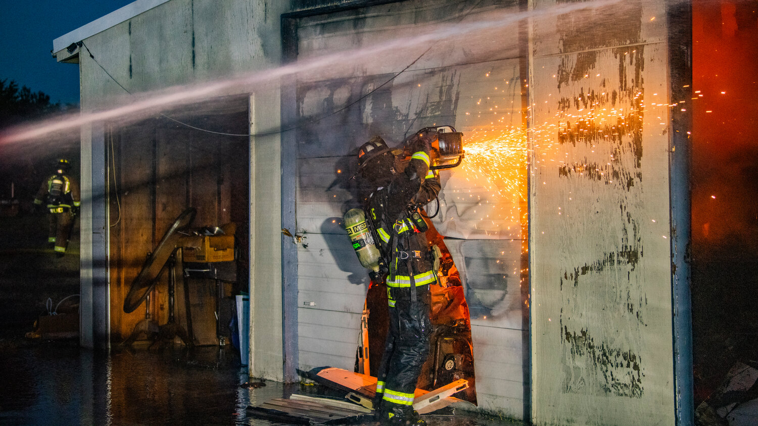 Lewis County Fire District 5 firefighter Wallace uses a saw to cut through a garage door as crews battle flames inside a structure near the 100 Block of Alder Avenue Northwest in Napavine on Saturday, June 3.