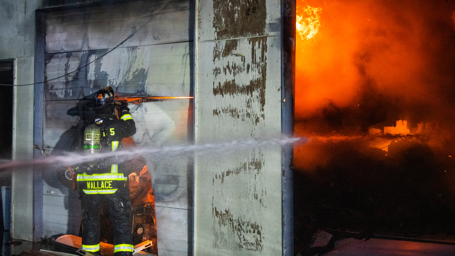 Lewis County Fire District 5 firefighter Wallace cuts through a garage door as crews battle flames inside a structure near the 100 Block of Alder Avenue Northwest in Napavine on Saturday, June 3.