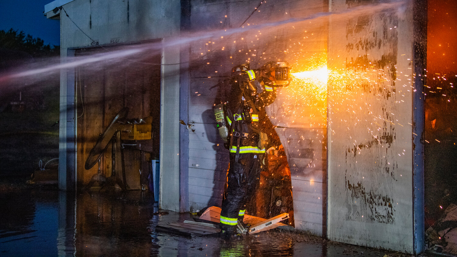 Lewis County Fire District 5 firefighter Matthew Wallace cuts through a garage door as crews battle flames inside a structure near the 100 Block of Alder Avenue Northwest in Napavine on Saturday, June 3.
