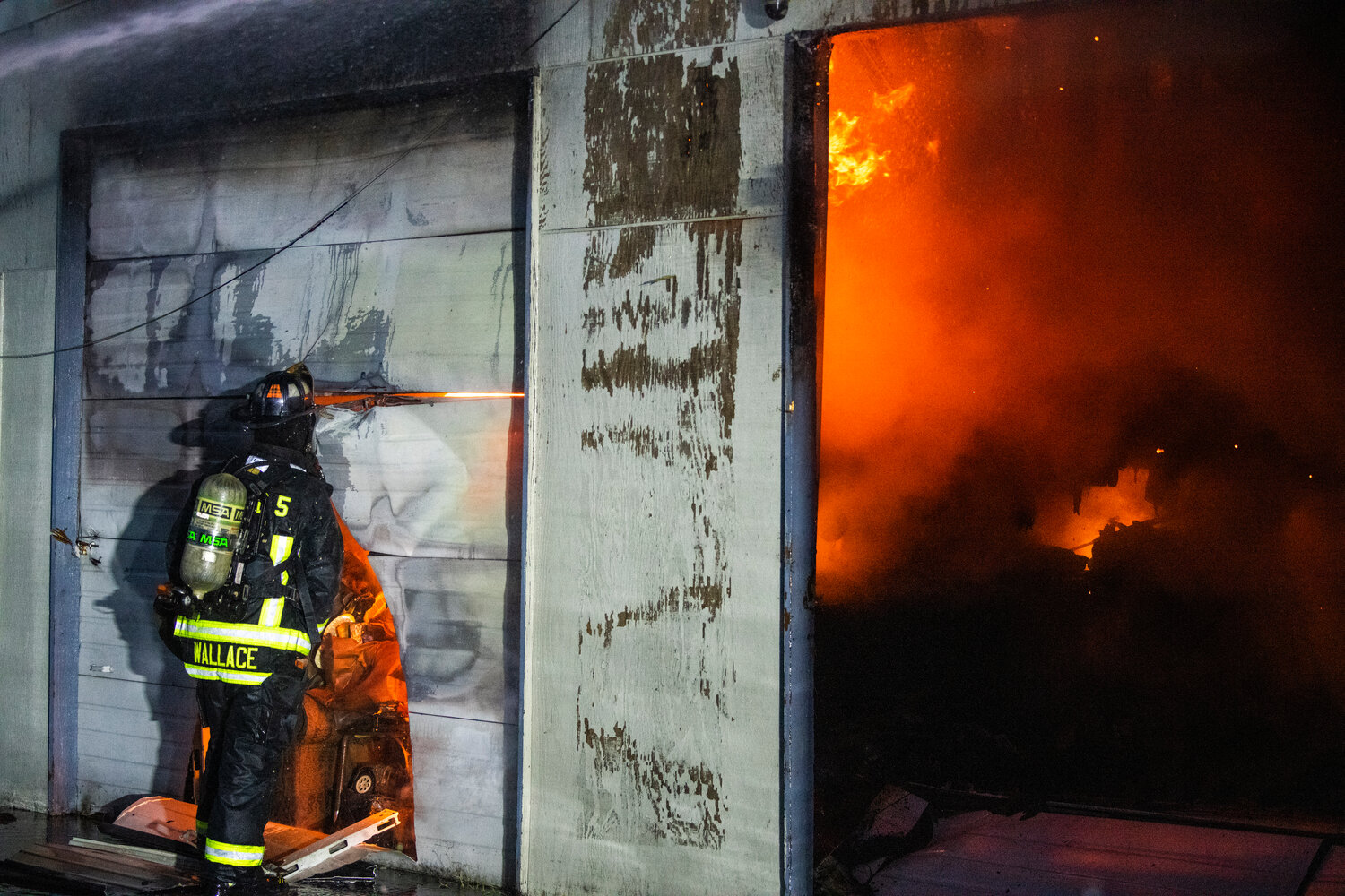 Lewis County Fire District 5 firefighter Matthew Wallace peers through a garage door as crews battle flames inside a structure near the 100 Block of Alder Avenue Northwest in Napavine on Saturday, June 3.