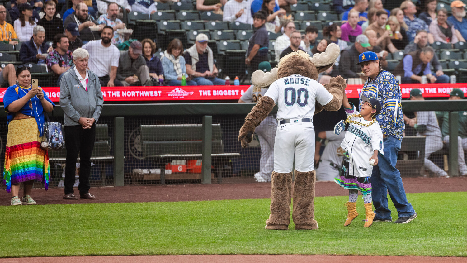 Payton KillEagle, a 7-year-old Mariners fan and cancer survivor, jumps up with her tongue out to high-five the Mariners Moose mascot after throwing out the first pitch as she is celebrated during Native American Heritage Night in Seattle on Monday, Aug. 28.