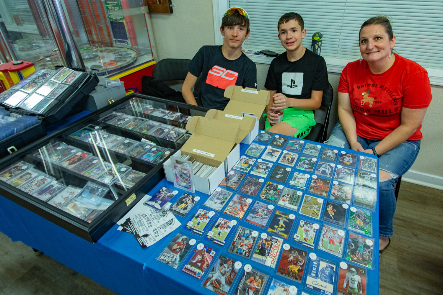 From left, Kolson Otis, of Mossyrock, Aiden Combs, of Roy, and Carrie Anderson, of Mossyrock, sit behind their table selling sports cards on Saturday, Sept. 2 at the inaugural Keiper's Cards and Memorabilia Show at the Tower Mall, located at 320 N. Tower Ave.
