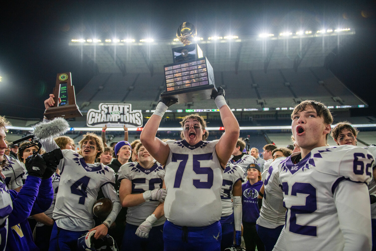 Anacortes lineman Kyle Leseman (75) hoists the 2A State Championship trophy high after the team’s first-ever state title win at Husky Stadium on Saturday, Dec. 2.