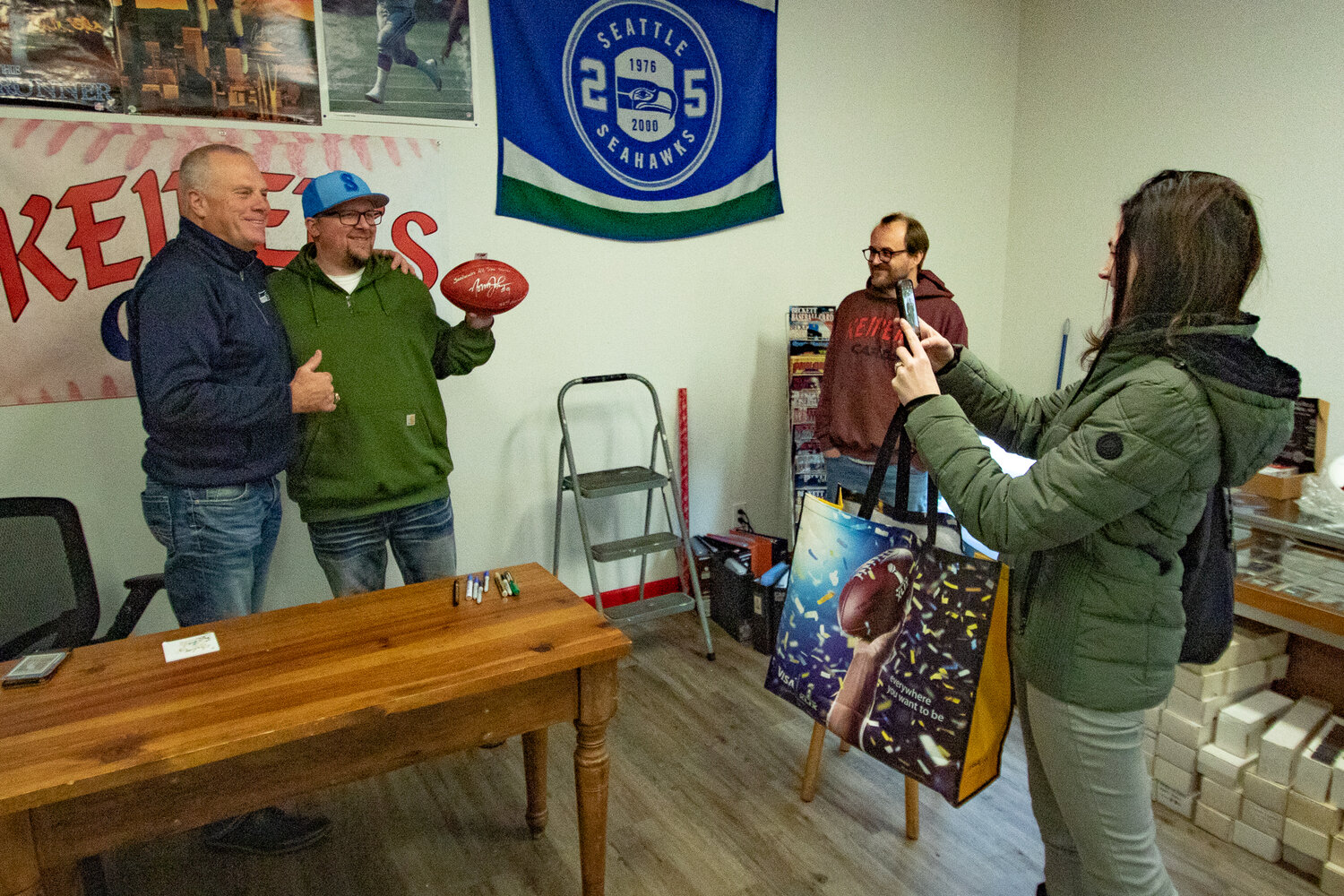 Former Seattle Seahawks kicker Norm Johnson, also known as "Mr. Automatic," poses with Brandon Maggs while Heidi Costello takes a picture after signing a football for Maggs at Keiper's Cards on Saturday, Dec. 2. during a card and memorabilia show in downtown Centralia.