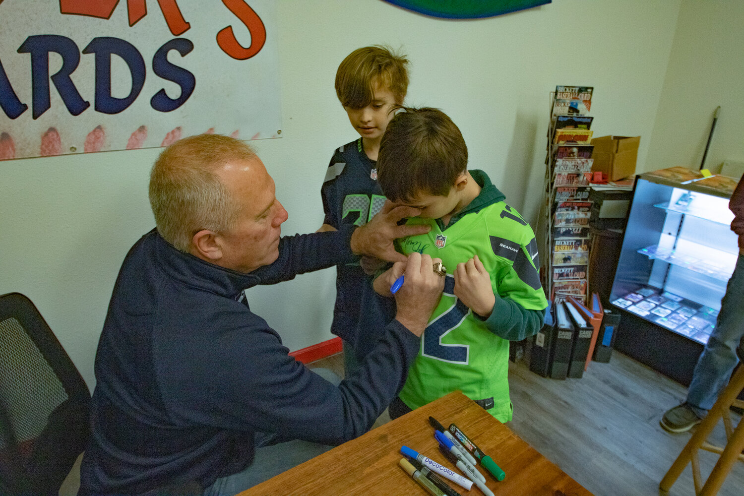 Cohen, in the green, and Bernard Collette, get their jerseys signed by Former Seattle Seahawks kicker Norm Johnson, also known as "Mr. Automatic," during the Keiper's Card and Memorabilia Show in downtown Centralia on Saturday, Dec. 2.