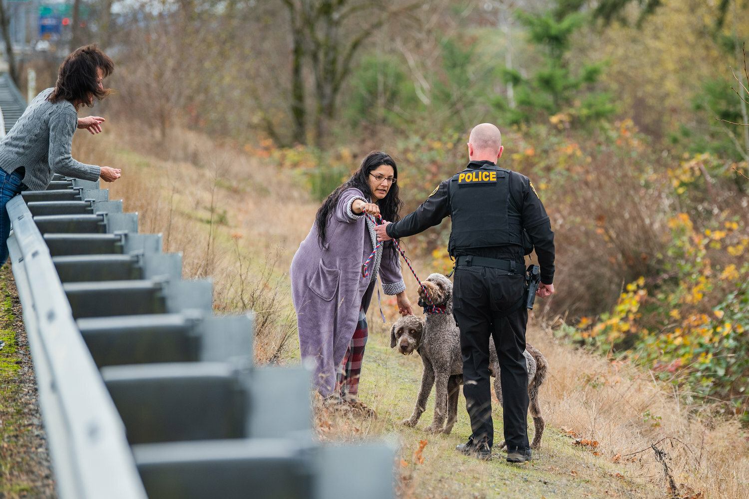 Maricruz Valencia, of Rochester, hands a leash to Officer M. King, with the Centralia Police Department, as April Thornton, of Centralia, holds treats in her hand for Buddy and Spike, two poodle-crosses who left their property along Russell Road in Centralia before walking through traffic near Interstate 5 in December 2022.